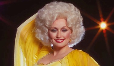 Dolly Parton wearing a yellow dress smiling at the camera.